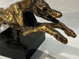 statue d'un chien courant sur un socle noir sur fond blanc