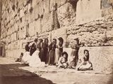 an old photo of a group of people sitting in front of a stone wall