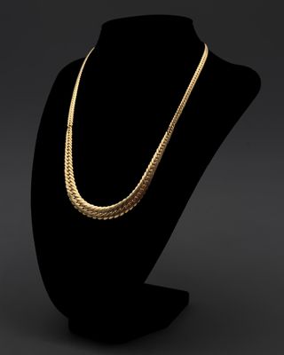 un collier en or posé sur un socle de mannequin noir
