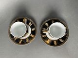 two cups and saucers with gold trims on a table