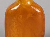 an orange glass snuff bottle with a metal cap on a gray surface