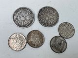 six types différents de pièces d'argent posées sur une surface blanche
