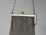 an antique silver mesh purse hanging from a chain on a gray wall