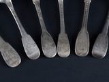 six silver spoons are lined up in a row on a black surface