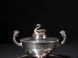 a silver plate with a bowl and saucer on a black surface