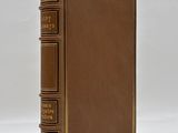 an old brown book with gold trim sitting on top of a white surface