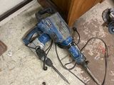 un marteau-piqueur bleu posé par terre à côté d'une paire de chaussures