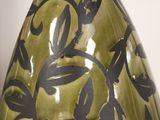 a green vase with black leaves on it sitting on a table