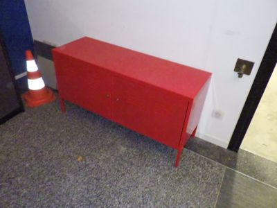 une armoire rouge dans un coin de la pièce, à côté d'un cône de signalisation