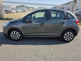 La voiture grise est garée sur le parking, à côté d'une clôture.