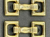 two gold buckles on a gray surface with a black background