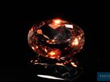 a close up of a fancy orange diamond on a black surface