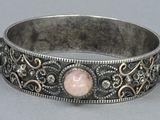 a close up of a silver bracelet with a pink stone on it