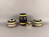 un vase noir et jaune ainsi que deux tasses et soucoupes posées sur une table