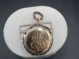 a close up of a gold pocket watch with a monogram on it
