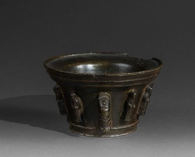 an old black bowl with carvings on it on a gray surface