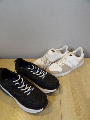 two pairs of black and white sneakers sitting on top of a wooden floor