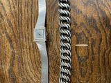a silver bracelet and a silver watch on a wooden table