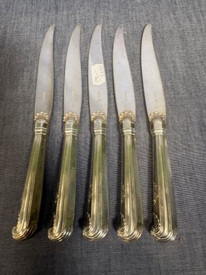 quatre couteaux en métal argenté et un porte-couteaux posés sur une table