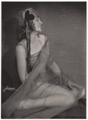 photographie en noir et blanc d'une femme en robe, assise sur un lit