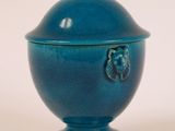 un petit bol bleu avec un couvercle, posé sur une surface blanche