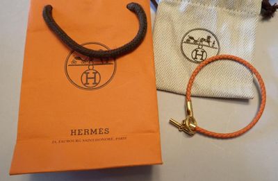 un sac Hermès orange orné d'une breloque dorée et d'un bracelet en cuir marron