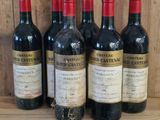 six bottles of wine are lined up on a wooden shelf