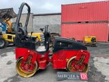 a red and black road roller parked in front of a red building