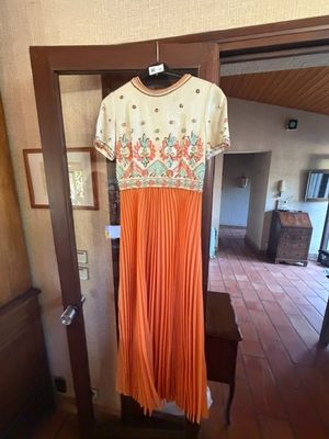 une robe plissée orange suspendue à un cintre dans une pièce