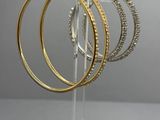 trois boucles d'oreilles en forme d'anneau, dorées et argentées, présentées sur un présentoir en acrylique transparent