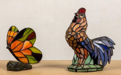 deux sculptures en vitrail représentant un coq et un papillon, posées sur une table