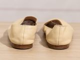 beige leather slippers on a wooden table with a white wall in the background