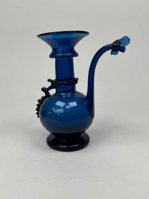 a blue glass vase with a black handle on a white table