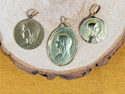 three silver and gold medals of jesus and mary on a wood slice