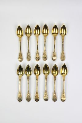 six cuillères en or sont disposées en rangée sur une surface blanche