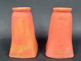une paire de vases orange posés sur une surface noire, avec un fond noir
