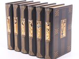 trois livres noirs aux tranches dorées sont alignés sur une surface blanche
