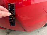 a person holding a ruler in front of a red car