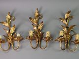 three gold leaf wall sconces mounted on a white wall