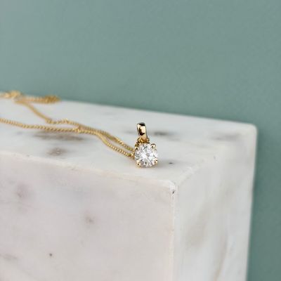the gold necklace is sitting on a marble block with a diamond on it