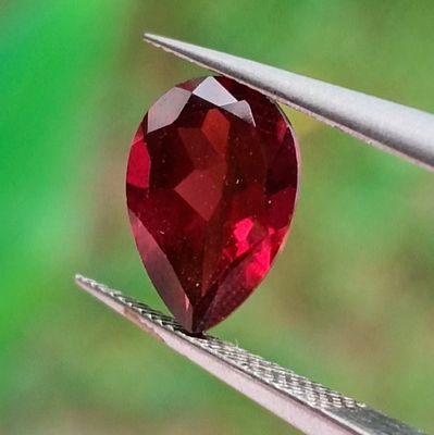 un gros plan sur un diamant rouge en forme de cœur tenu par une paire de pinces