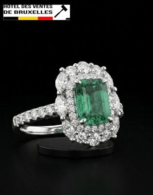 a close up of a green emerald and diamond ring on a black surface