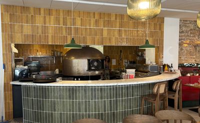 des tables et des chaises dans un restaurant doté d'un comptoir, avec un four à pizza à l'arrière