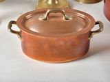 several copper pots and pans on a white table with a candle