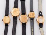 five watches are lined up on a white surface with a black strap