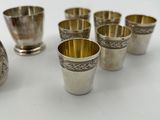 six silver cups and a pitcher on a white surface