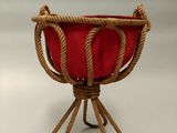 jardinière en corde avec un coussin rouge posée sur un support, sur fond blanc