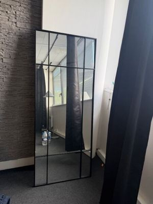 un grand miroir dans un coin de la pièce, près d'une fenêtre