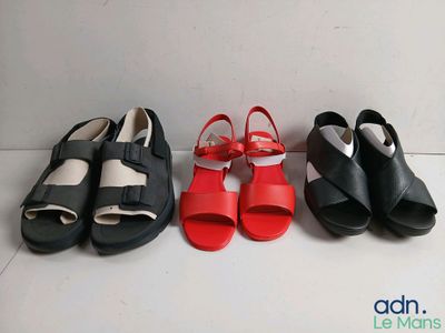 Trois paires de sandales noires, rouges et blanches sont alignées sur une surface blanche