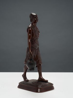 une statue en bronze représentant une femme tenant un pot posé sur une table
